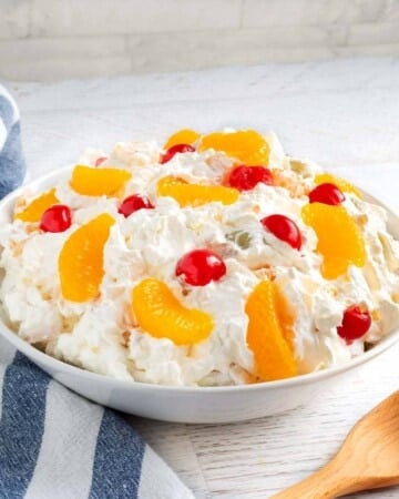 Creamy Fruit Salad in a white bowl with wood spoon and striped napkin.