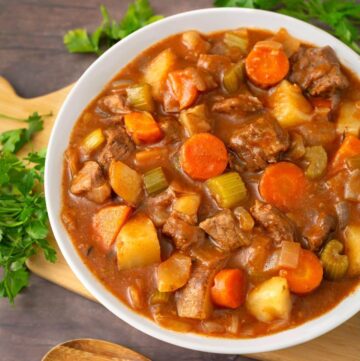 Beef Stew in a white bowl on a wooden board next to fresh parsley