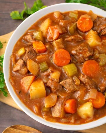 Beef Stew in a white bowl on a wooden board next to fresh parsley