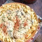 Creamy Chicken Breasts topping noodles in a beige bowl on top of a floral napkin