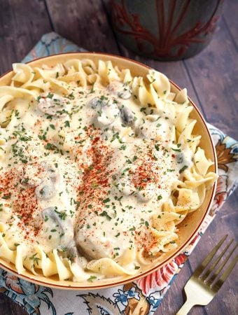 Creamy Chicken Breasts topping noodles in a beige bowl on top of a floral napkin