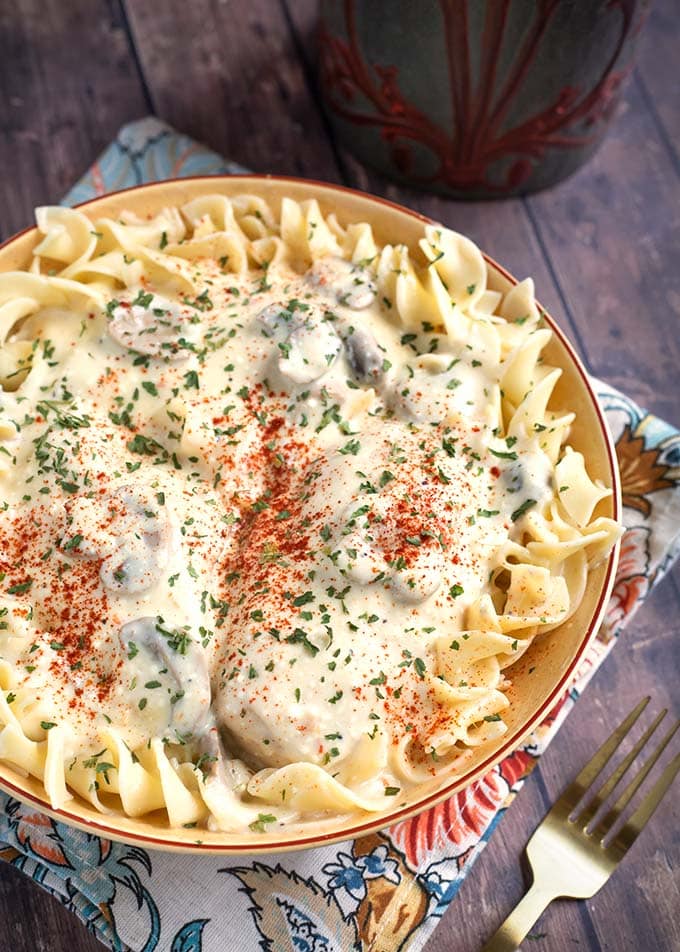 Creamy Chicken Breasts topping noodles in a beige bowl on top of a floral napkin