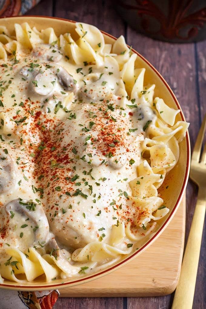 Close up of Creamy Chicken Breasts topping noodles in a beige bowl on top of a wooden board