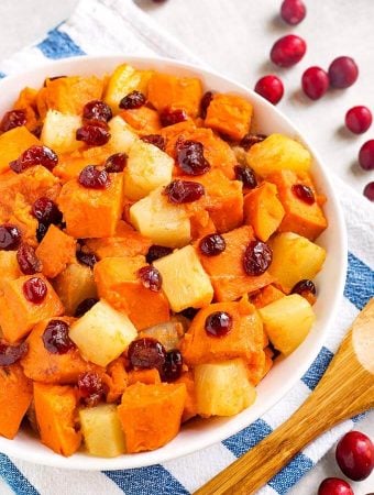 Closeup of Sweet Potato Cranberry Casserole in a white bowl on a white and blue napkin next to a wooden spoon