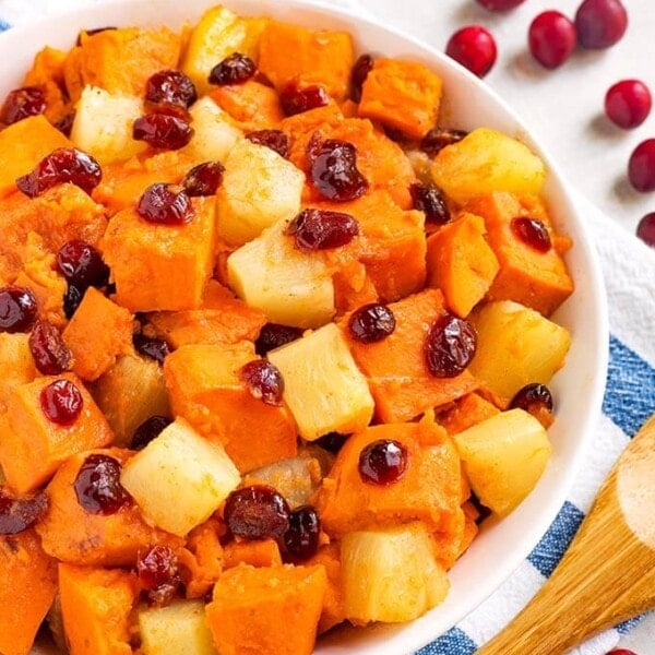 Closeup of Sweet Potato Cranberry Casserole in a white bowl on a white and blue napkin next to a wooden spoon