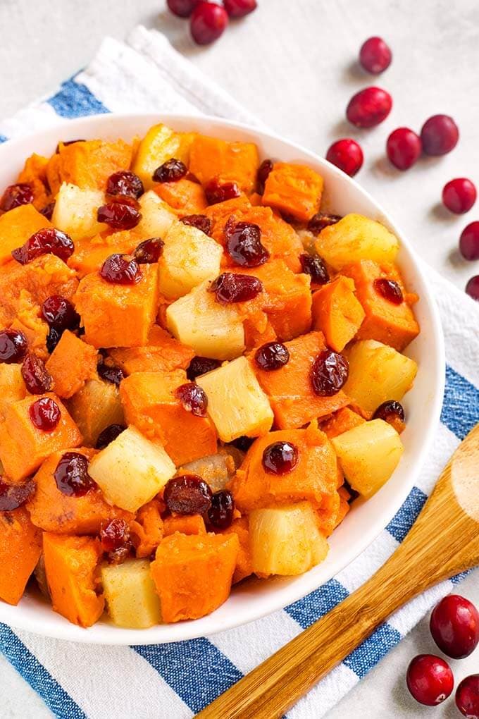 Closeup of Sweet Potato Cranberry Casserole in a white bowl on a white and blue napkin next to a wooden spoon