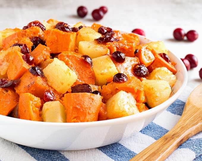 Side view of Sweet Potato Cranberry Casserole in a white bowl on a white and blue napkin next to a wooden spoon