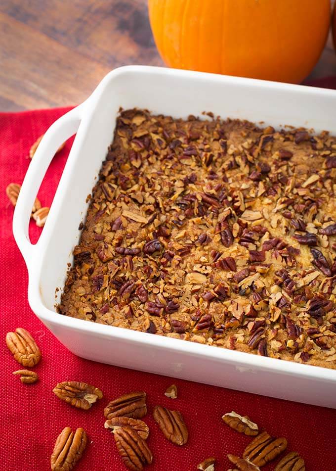 Pumpkin Pie Dump Cake in a white bakin dish on a red napkin with shelled pecans