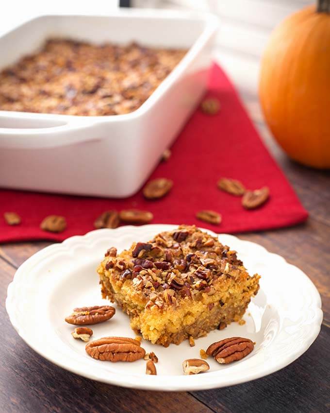 Slice of Pumpkin Pie Dump Cake on a white plate with pecan halves in front of white baking dish with remaining cake