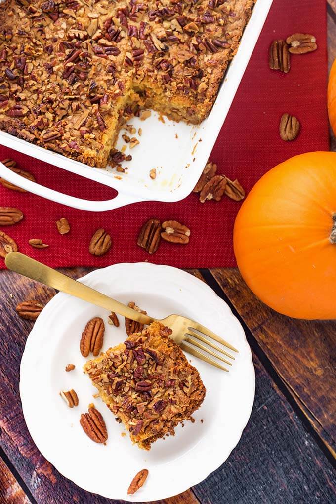 Top view of a slice of Pumpkin Pie Dump Cake on a white plate in front of white baking dish with remaining cake