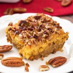 Slice of Pumpkin Pie Dump Cake on a white plate with pecan halves