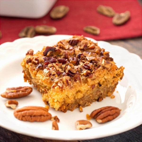 Slice of Pumpkin Pie Dump Cake on a white plate with pecan halves