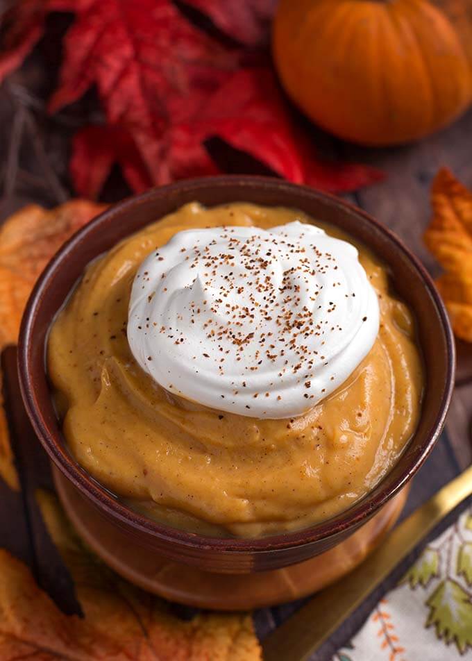 Quick Pumpkin Pie Pudding topped with a dollop of whipped cream in a wooden bolwon wooden coasters in front of red and orange leaves and pumpkins