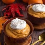 Quick Pumpkin Pie Pudding topped with a dollop of whipped cream on wooden coasters in front of red and orange leaves and pumpkins