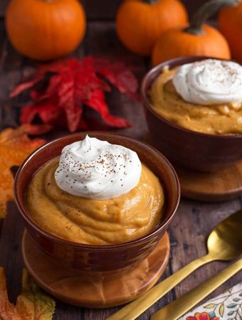 Quick Pumpkin Pie Pudding topped with a dollop of whipped cream on wooden coasters in front of red and orange leaves and pumpkins