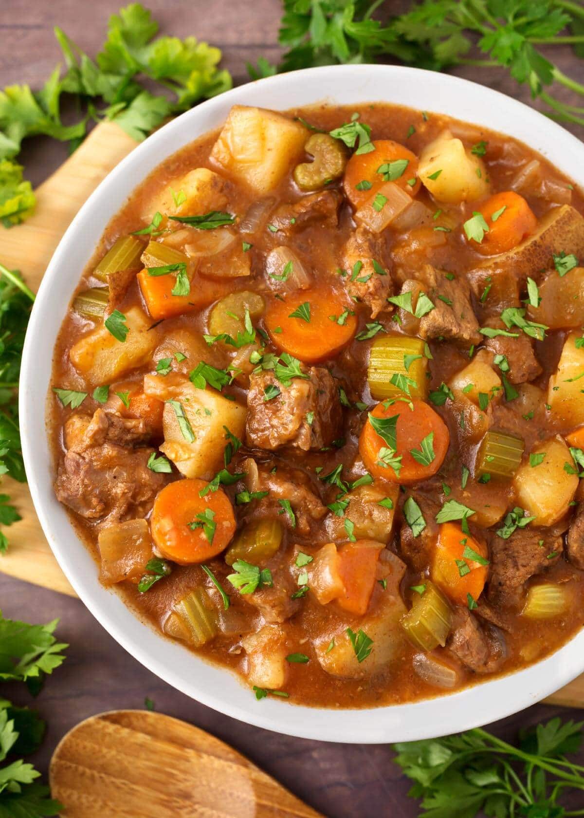 Beef Stew in a white bowl on a wooden board next to fresh parsley