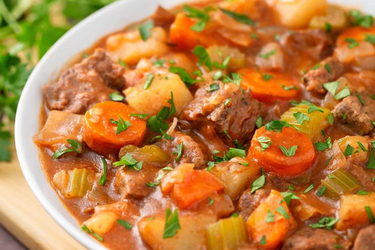 Beef Stew in a white bowl on a wooden board next to fresh parsley