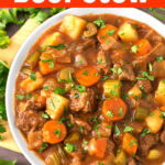 Beef Stew in a white bowl on a wooden board next to fresh parsley