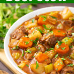 Beef Stew in a white bowl on a wooden board next to fresh parsley