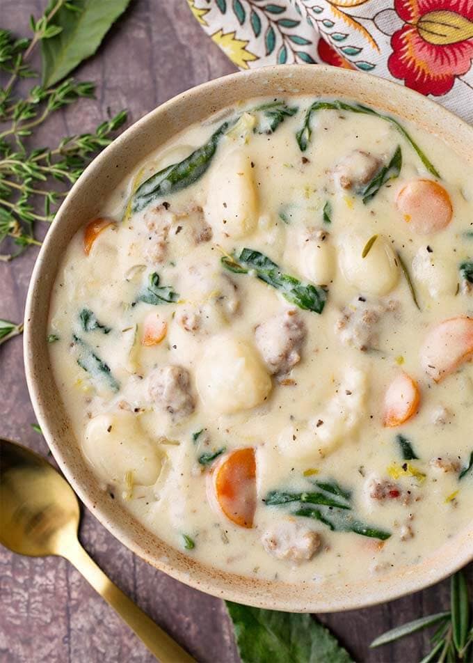 Creamy Sausage Gnocchi Soup in a beige bowl next to a golden spoon