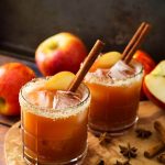 Two Apple Butter Old Fashioned Cocktails in glasses with salted rim on a wooden board with spices and apples