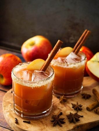 Two Apple Butter Old Fashioned Cocktails in glasses with salted rim on a wooden board with spices and apples