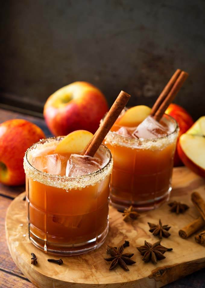 Two Apple Butter Old Fashioned Cocktails in glasses with salted rim on a wooden board with spices and apples