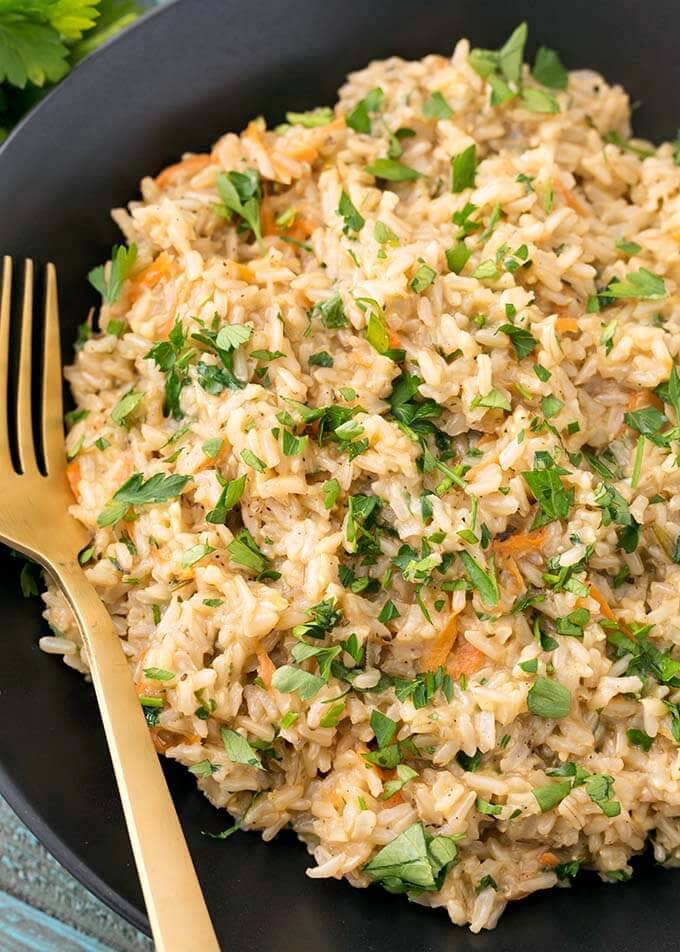 Closeup of Brown Rice Pilaf in a black bowl with gold fork