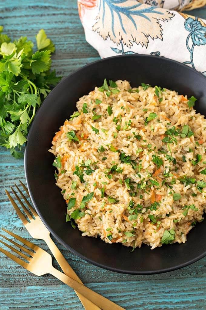 Brown Rice Pilaf in a black bowl next to floral napkin and bunch of fresh parsley