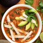 Chicken Tortilla Soup in a white bowl topped with tortilla strips, sliced avocados, and cilantro