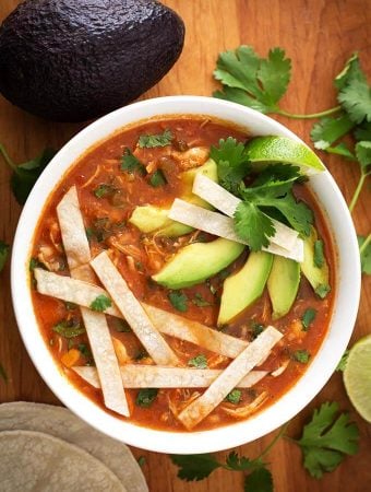 Chicken Tortilla Soup in a white bowl topped with tortilla strips, sliced avocados, and cilantro