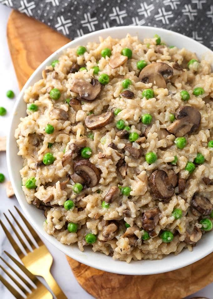 Mushroom Risotto with Peas on a white plate on a wooden board next to two golden forks