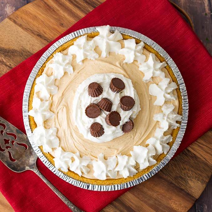 Top view of a No Bake Peanut Butter Pie topped with whipped cream and chocolate candies all on a red napkin next to a silver serving spoon