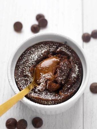 Chocolate Lava Cake in a white ramekin with golden spoon all on a light colored background