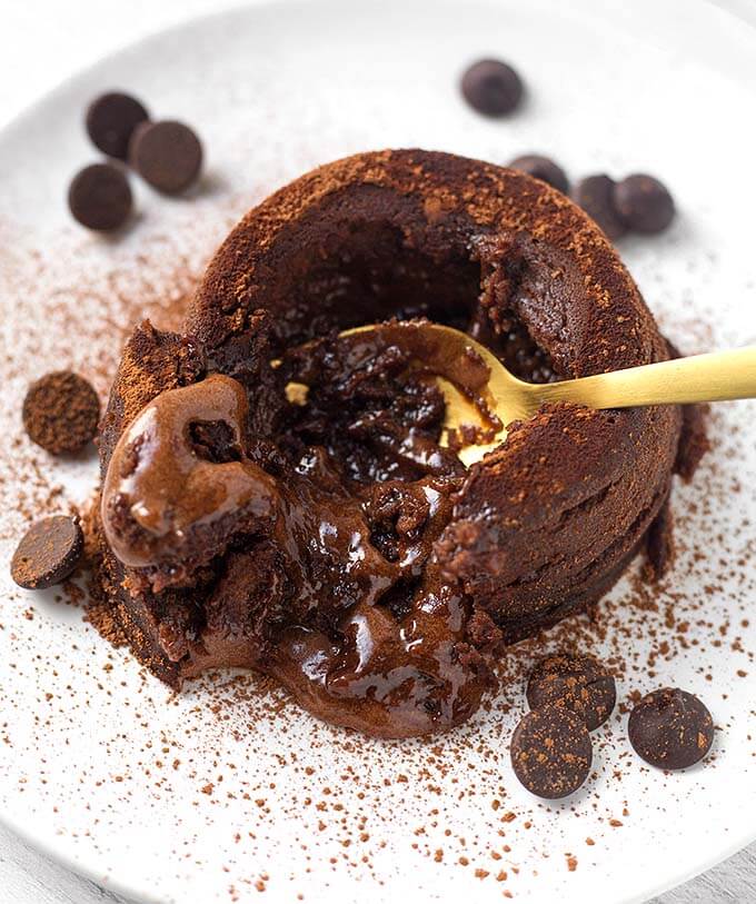 Gold spoon digging into Chocolate Lava Cake on a white plate with chocolate chips