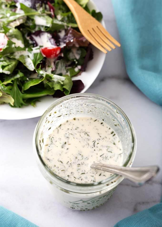 Small glass jar with Homemade Ranch Dressing next to a salad on a white plate