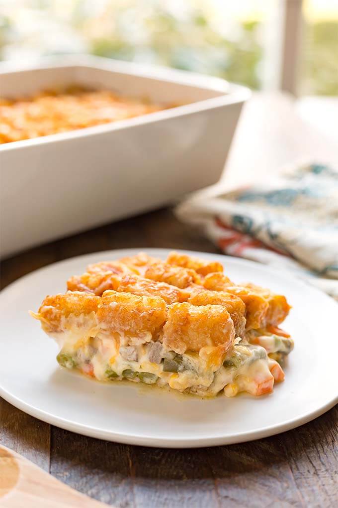 Slice of Hotdish Tater Tot Casserole on a white plate in front of white baking dish