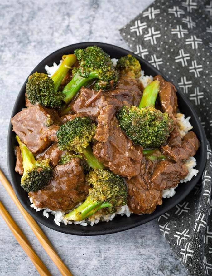 Beef and Broccoli in a black bowl next to two wooden chosticks and a black and white patterned napkin