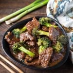 Beef and Broccoli in a black bowl next to two wooden chosticks and a black and white patterned napkin