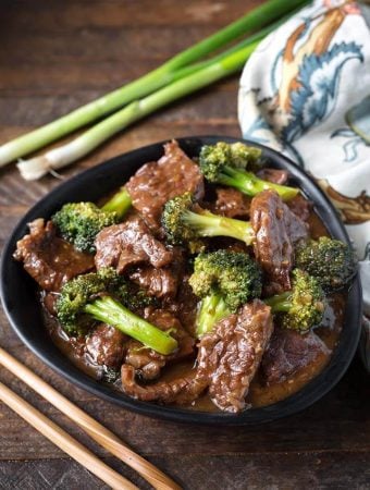 Beef and Broccoli in a black bowl next to two wooden chosticks and a black and white patterned napkin