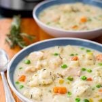 Two white and blue bowls of Chicken and Dumplings on a wooden board next to spoon