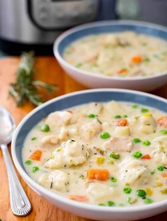 Two white and blue bowls of Chicken and Dumplings on a wooden board next to spoon