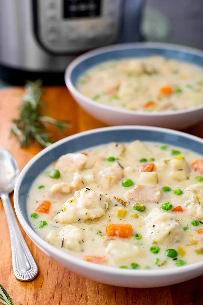 Two white and blue bowls of Chicken and Dumplings on a wooden board next to spoon