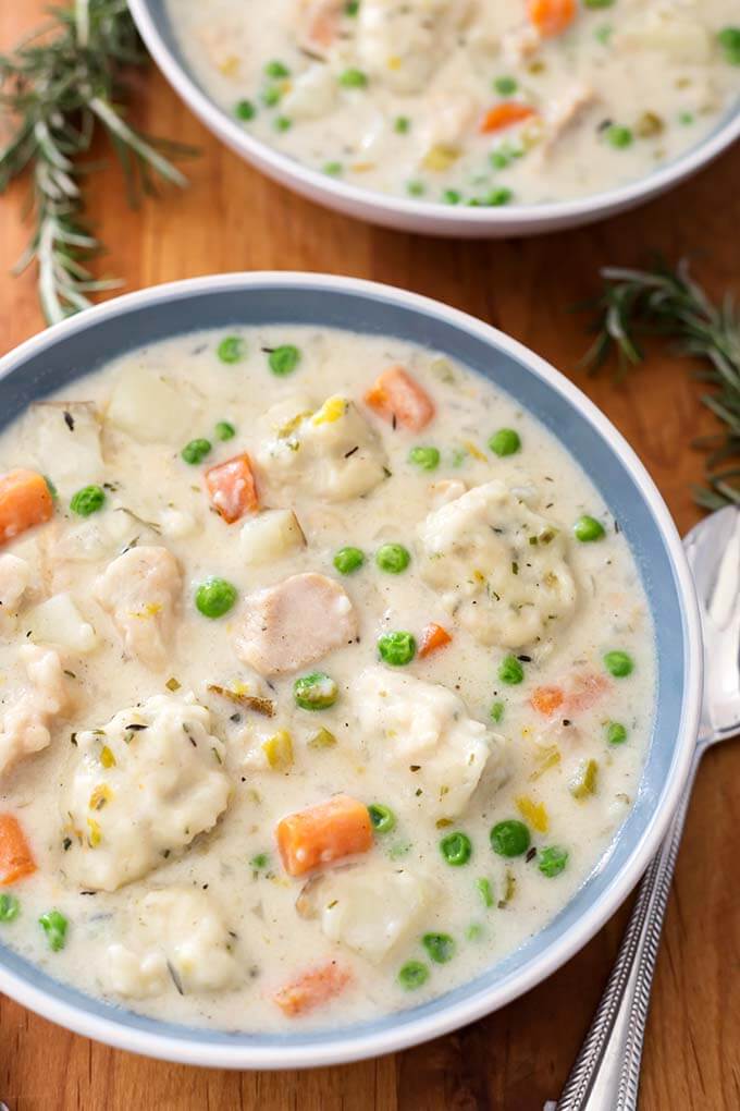 Two white and blue bowls of Chicken and Dumplings on a wooden board next to spoon