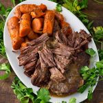 Pot Roast and carrots on a white oblong platter surrounded by fresh parsley