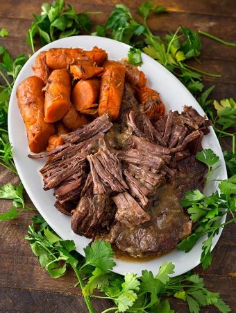 Pot Roast and carrots on a white oblong platter surrounded by fresh parsley