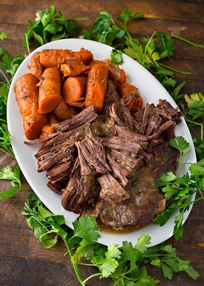 Pot Roast and carrots on a oblong white platter surrounded by fresh parsley