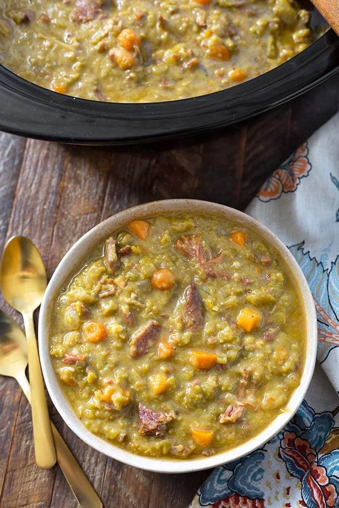 Split Pea Soup in a beige bowl next to two gold spoons in front of slow cooker