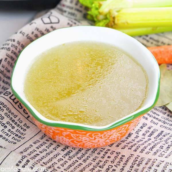 easy chicken bone broth in orange bowl with green rim on top of news-typed napkin
