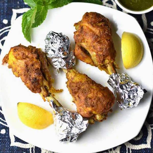 Tandoori Chicken with foil on ends of bone on a white plate with lemon wedges 